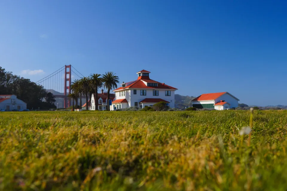 Green lawn with historic buildings and Golden Gate Bridge in background in Presidio national park site in San Francisco, California.